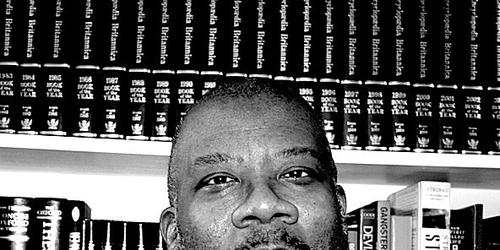black and white image of Dr Kenny Monrose into front of a book shelf